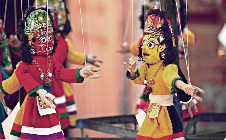 Traditional colorful Rajasthani string puppets (Kathputli) dressed in bright red and yellow clothes with painted wooden faces and intricate headgear, hanging on strings and used in folk performances.